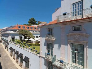 A building with a balcony, a garden with umbrellas, and a tree.