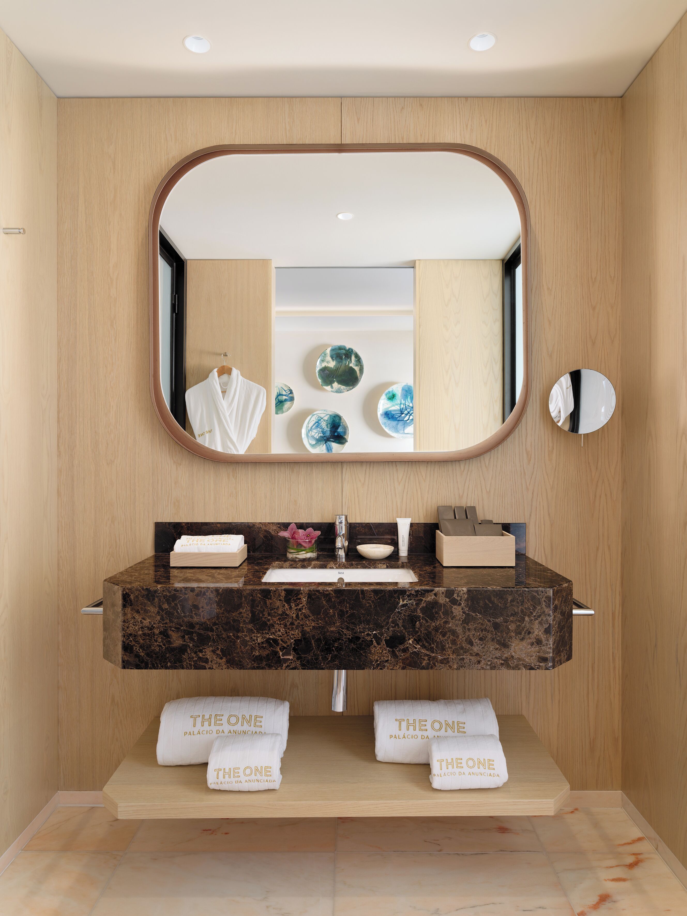 A modern bathroom with a marble sink, two towel racks with branded towels, a large mirror, and decorative plates.