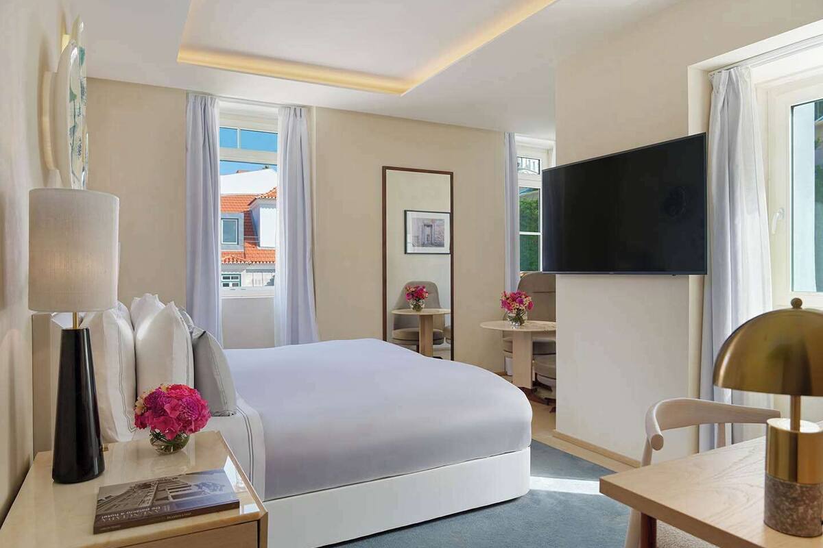 A hotel room with a bed, a desk, a television, and a small table with flowers.