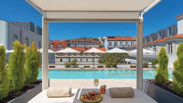A rooftop terrace with a pool, sun loungers, and a table with a fruit platter and a glass of wine.