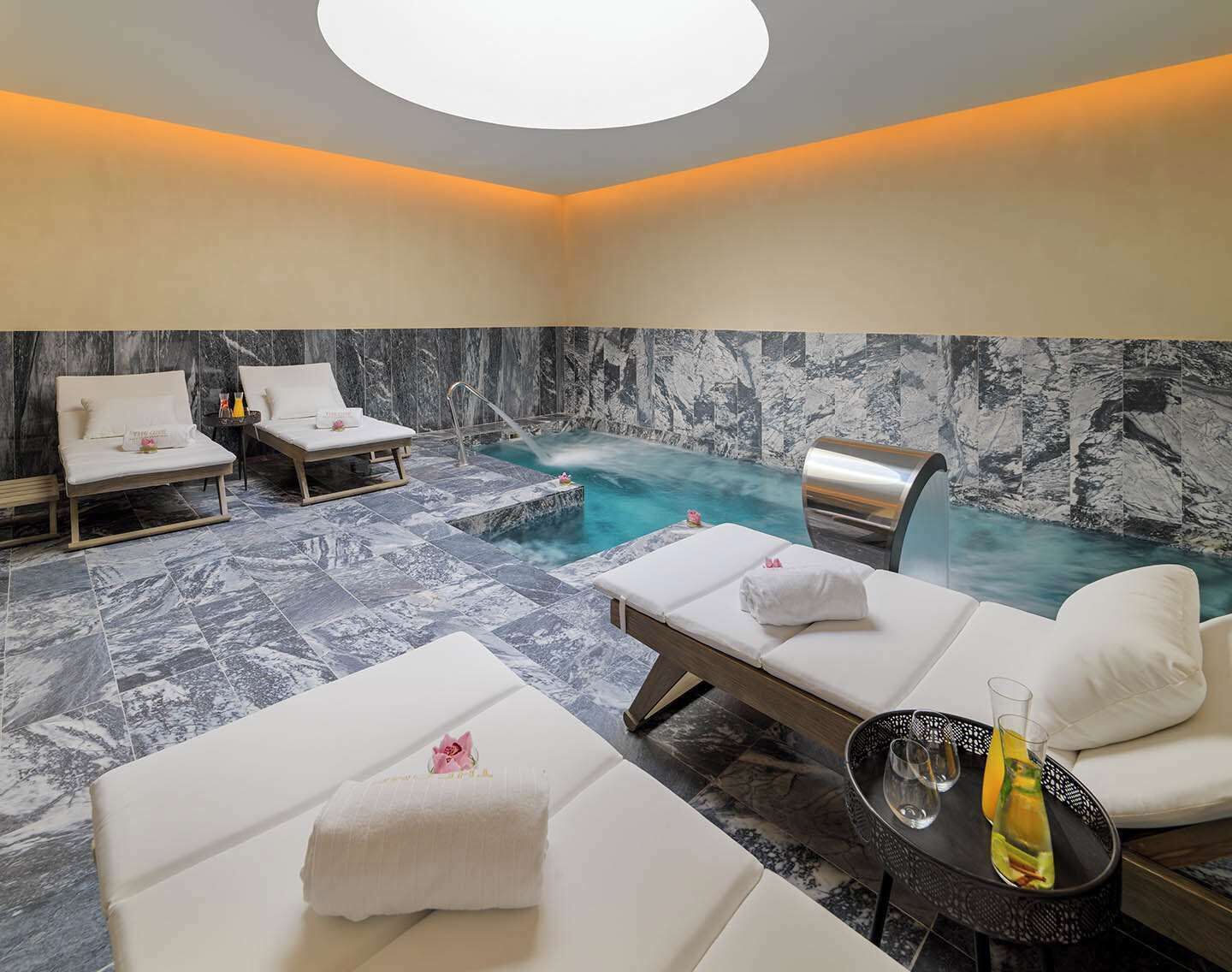 Une salle de spa avec un mur en marbre, un jacuzzi et deux fauteuils confortables.