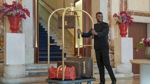 A person pushing a luggage cart with suitcases and bags in a lobby with marble flooring and ornate wall decorations.