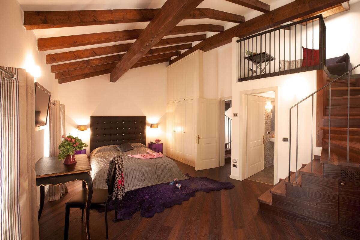 A bedroom with a large bed, a desk, a chair, a dresser, and a staircase.
