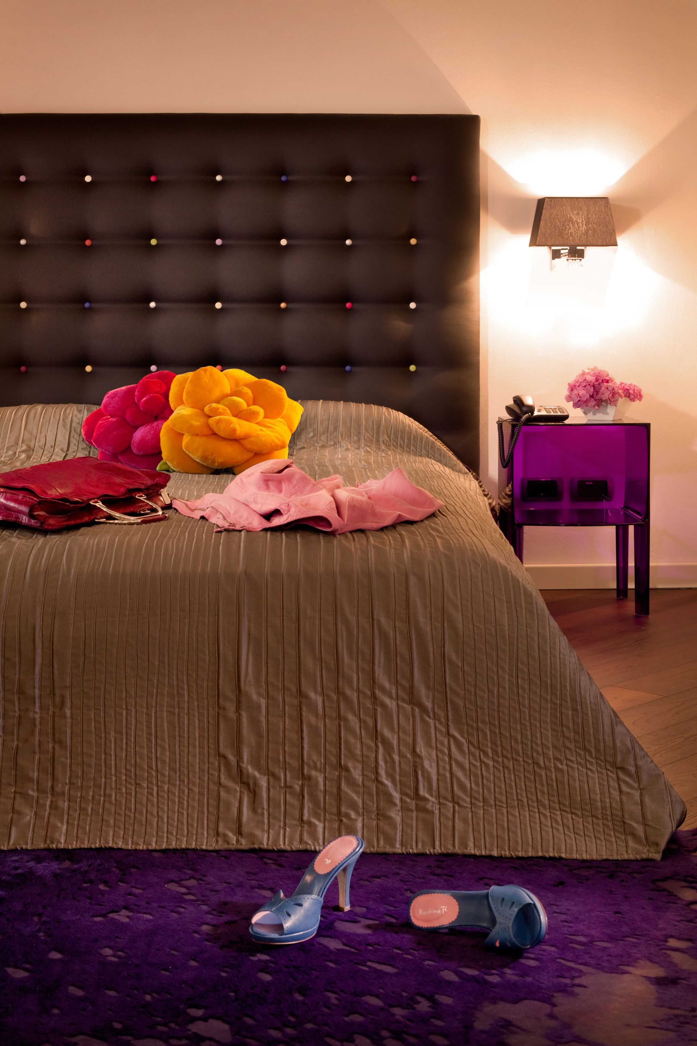 A bedroom with a tufted headboard, a bedside table with a lamp, and a purple chair.