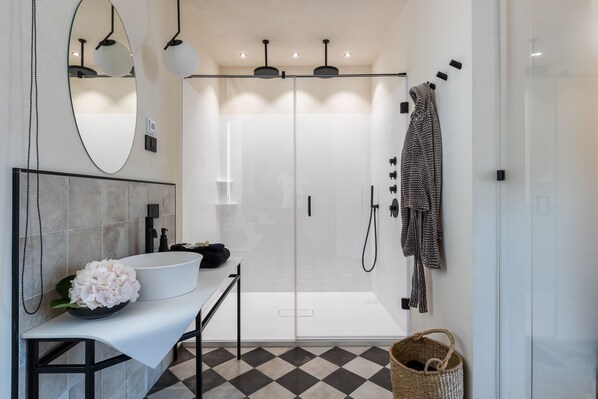 Un baño moderno con un lavamanos blanco, un espejo grande y una ducha con cerramiento de vidrio.