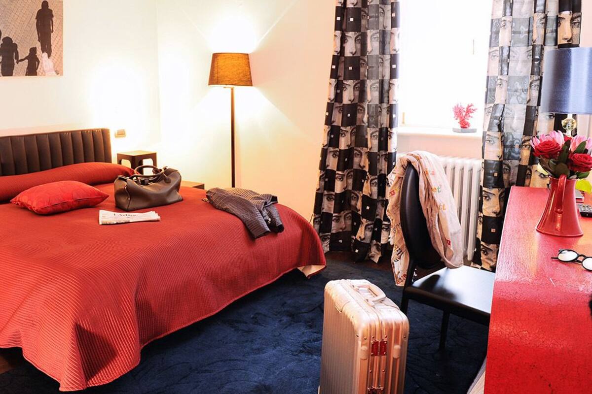 A hotel room with a large bed, a bedside table with a lamp, a suitcase, and a chair.