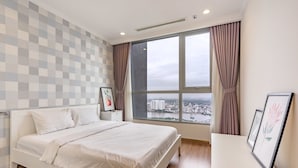 A bedroom with a large window, a bed, a bedside table, and a view of a cityscape. - Zahoo House - Vinhomes Central Park (Ho Chi Minh City)