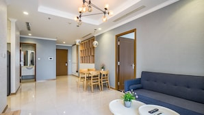 A modern living room with a sofa, two coffee tables, a dining area with a table and chairs, and a kitchen area with a refrigerator and cabinets. - Zahoo House - Vinhomes Central Park (Ho Chi Minh City)