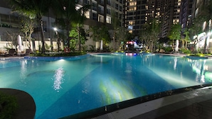 A nighttime swimming pool with clear water, surrounded by palm trees and a high-rise building in the background. - Zahoo House - Vinhomes Central Park (Ho Chi Minh City)