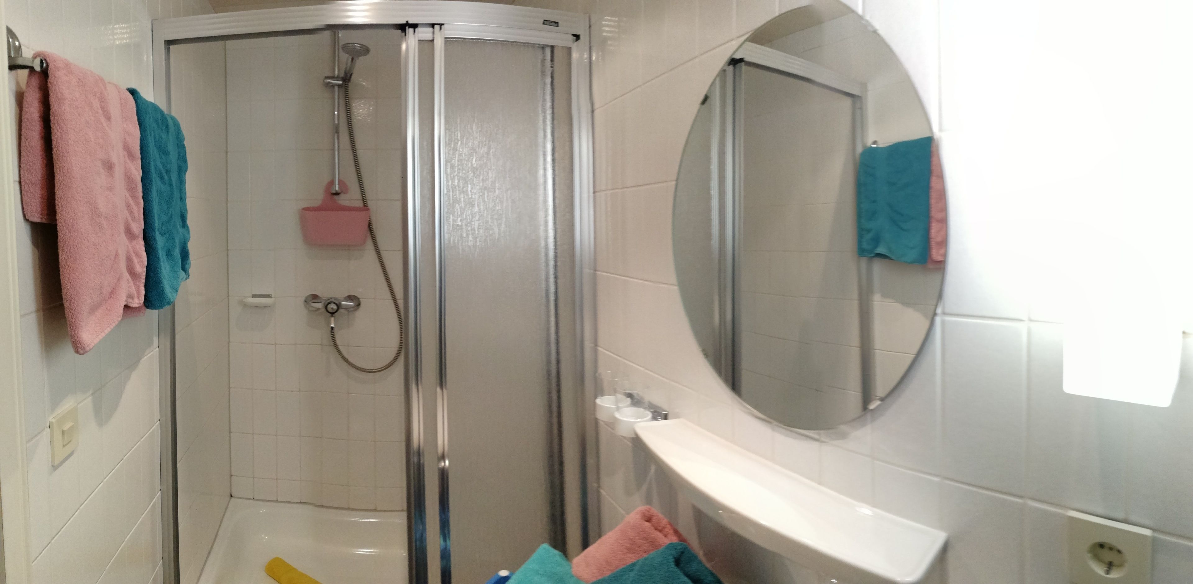 Ein Badezimmer mit Duschkabine, weißem Waschbecken und Spiegel.
