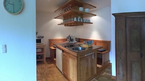 Una cocina con armarios de madera, un lavamanos y una encimera. Hay una repisa sobre el lavamanos con tazas y vasos.