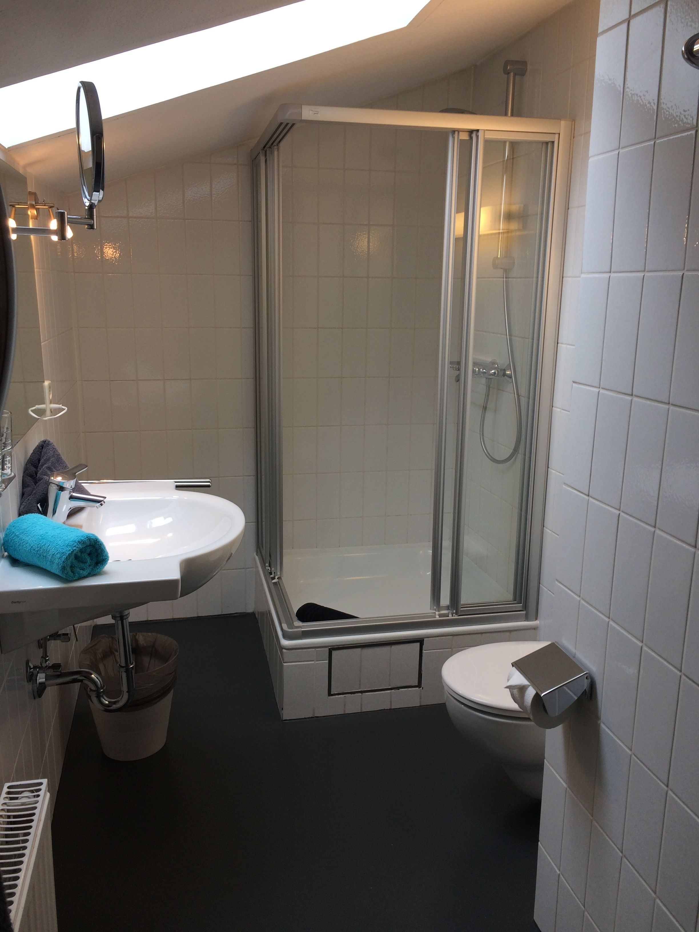 Ett modernt badrum med en dusch som är avskärmad med glasväggar, ett handfat med spegel och en toalett.