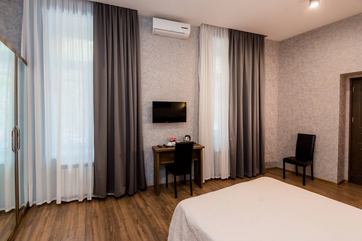 A hotel room with a bed, a desk with a chair, a TV mounted on the wall, and a door.