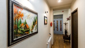 Un pasillo con un cuadro enmarcadosiendo un paisaje montañoso, un radiador y una puerta con decoraciones coloridas.