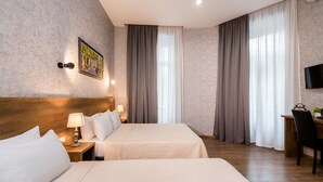Habitación de hotel con dos camas, cabecera de madera, escritorio con silla, televisor y ventana con cortinas.