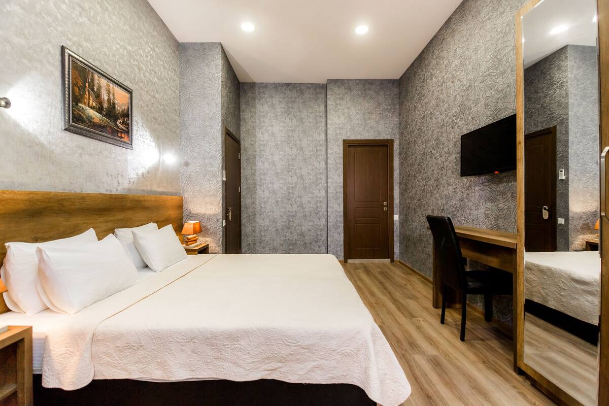 A neatly arranged bedroom with a bed, a desk, a chair, a TV, and a door.