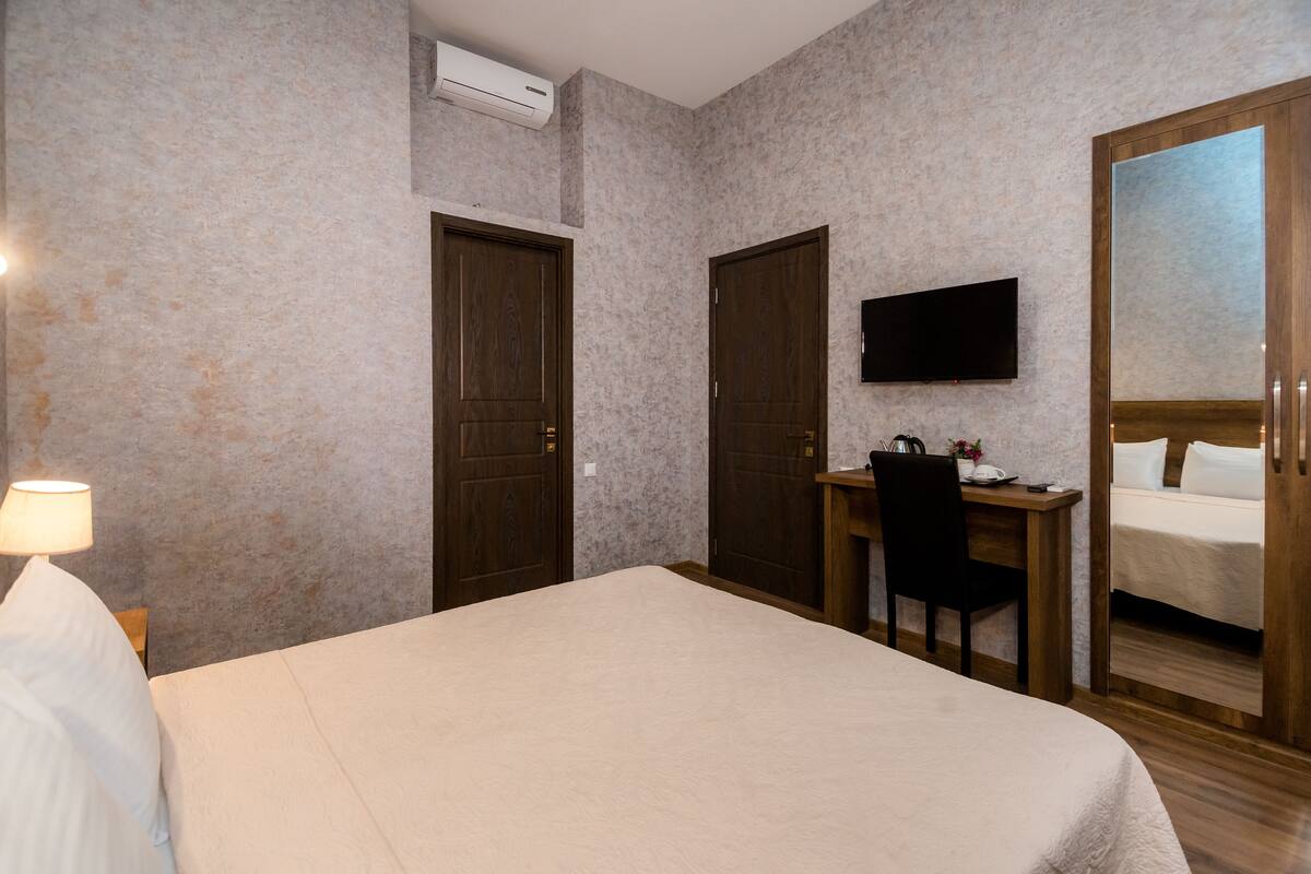 A hotel room with a bed, a desk with a chair, a television, and a wardrobe.