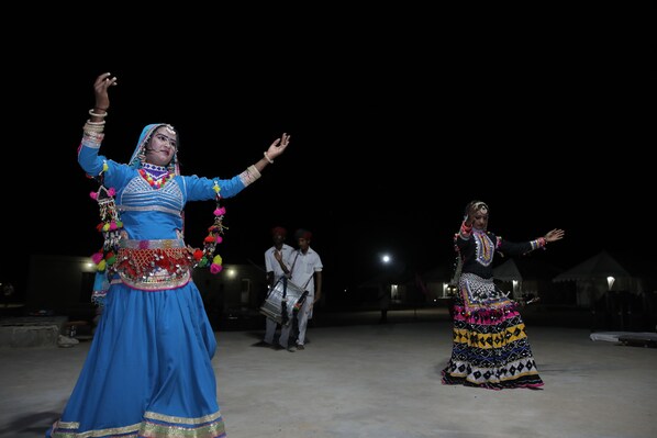 Two performers in traditional attire dancing on a stage with a dark background.