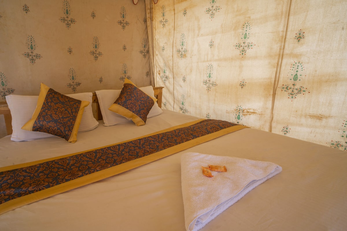 Una cama bien hecha con un corredor estampado, almohadas y una toalla doblada en una habitación de hotel.