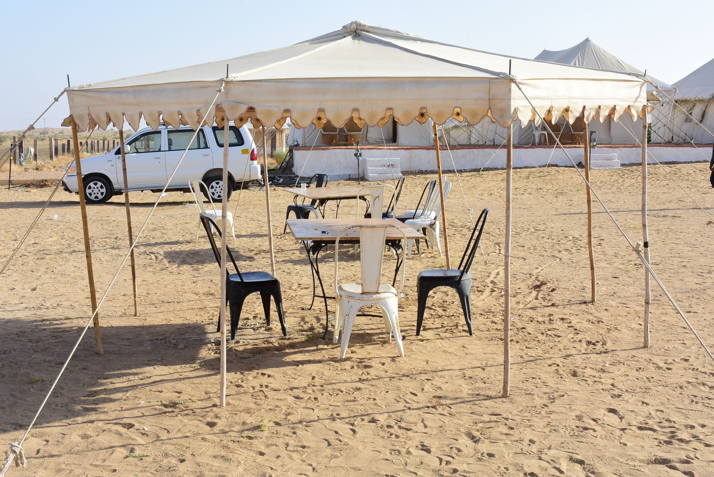 A desert campsite with a large tent, a dining table, and chairs.