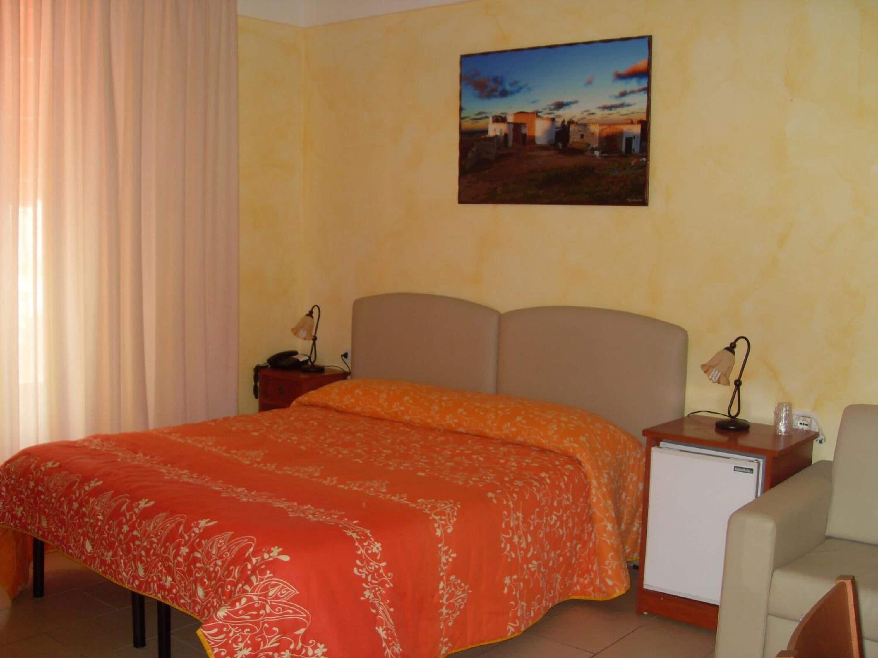 Habitación de hotel con cama, mesita de noche, escritorio, silla y un cuadro colgado en la pared.