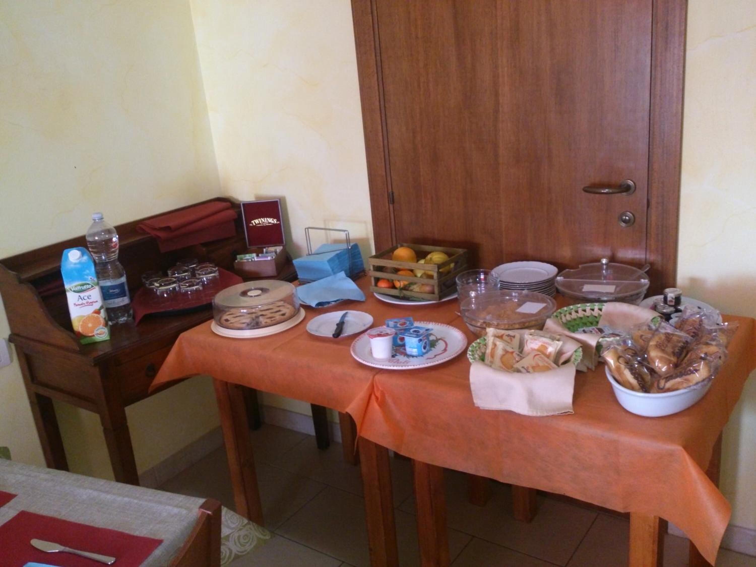 Una mesa dispuesta con diversos alimentos y bebidas, incluyendo un pastel, fruta y aperitivos envasados.