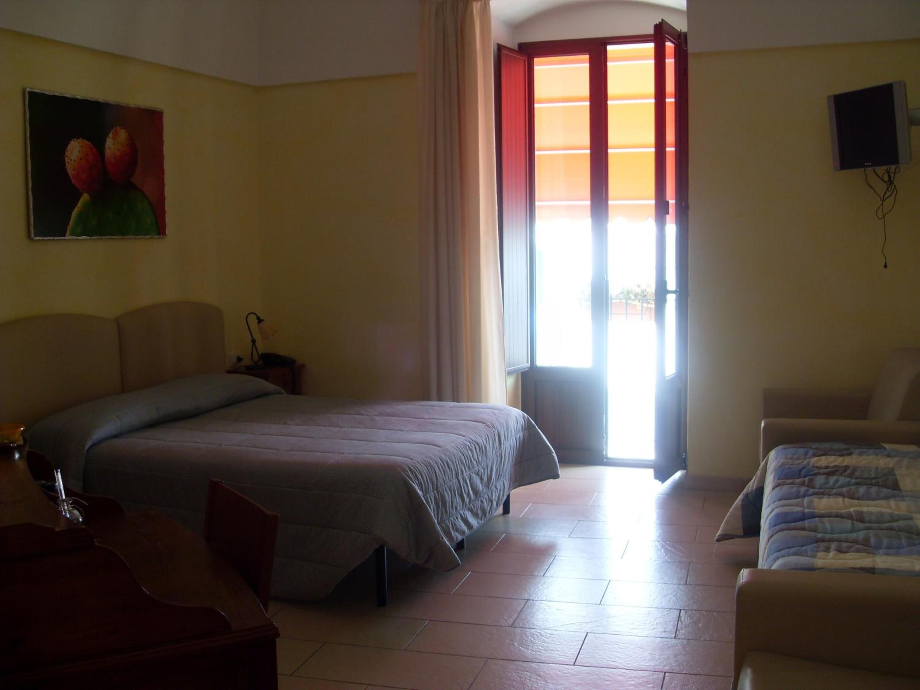 Una habitación de hotel con una cama, una silla, un escritorio, un cuadro y un televisor.