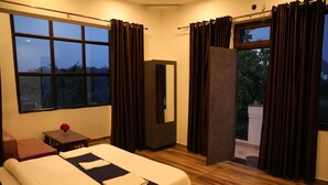 A hotel room with a bed, a small table with a vase of flowers, a mirror, and a view of the outdoors through a door. - Winter Mountain Resort (Pushkar)