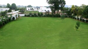 A large, open grassy area with a few trees and white buildings in the background. - Winter Mountain Resort (Pushkar)
