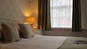 A neatly made bed with pillows, a bedside lamp, and a window with curtains.