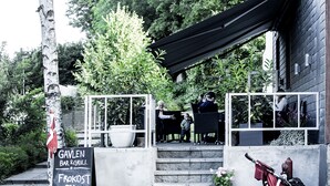 Un restaurant avec une terrasse, une enseigne, une poussette et un arbre.