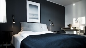Une chambre d’hôtel moderne, avec un lit, des lampes de chevet, un tableau encadré au mur et une petite table sur laquelle est posée une plante.