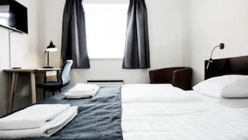 Habitación de hotel con cama, escritorio, silla, televisor y ventana con cortinas.