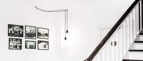 A staircase with wooden steps and a dark handrail, leading to a white door. A black and white sofa is positioned against the wall, and several framed pictures are displayed above it.