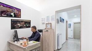 A man working at a desk with a computer, a clock, and framed pictures on the wall. - Opera Home Principe Umberto (Naples)