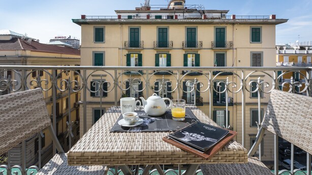 A balcony with a table set for breakfast, including a teapot, cups, and a glass of orange juice. - Opera Home Principe Umberto (Naples)