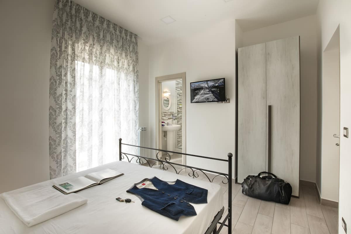 A bedroom with a bed, a bedside table, a wardrobe, a mirror, and a window with curtains.