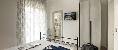 A bedroom with a bed, a bedside table, a wardrobe, a mirror, and a window with curtains.