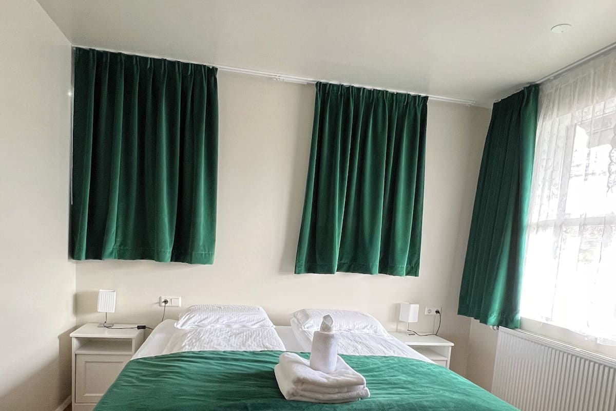 Une chambre d’hôtel avec un grand lit, des rideaux verts, du linge de lit blanc et un radiateur.