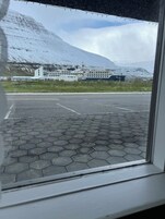 Vista de un edificio con un gran barco amarrado al frente, un estacionamiento con pavimento hexagonal y montañas al fondo.
