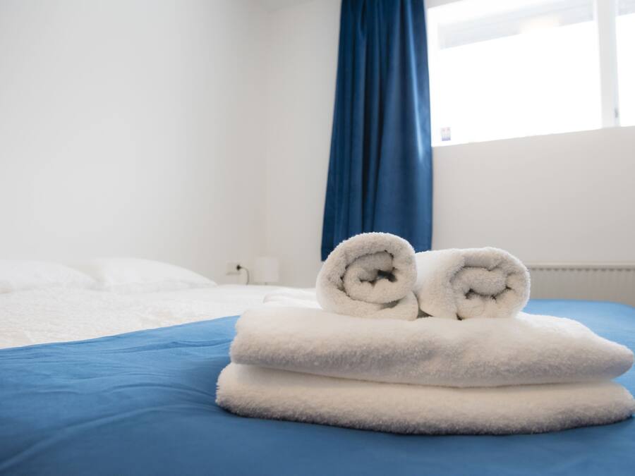 Ein ordentlich bezogenes Bett mit blauer Bettwäsche und zwei aufgerollten weißen Handtüchern darauf.