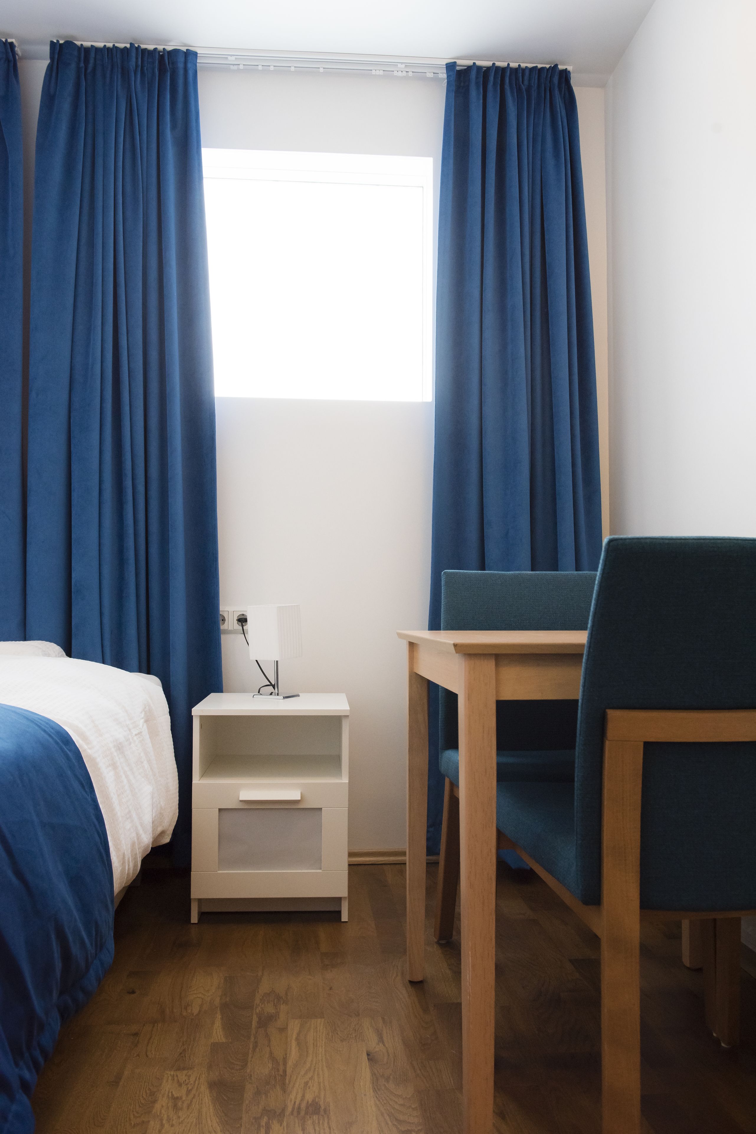 A room with a bed, a nightstand, a table, and a chair.