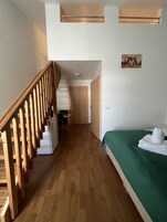 Una habitación de hotel con una escalera de madera, una cama con colcha verde y una pequeña kitchenette.
