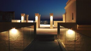 A nighttime view of a building's exterior with illuminated pillars and a staircase leading to a balcony. - Monun Hotel & Spa  (Grottaglie)