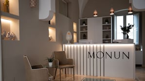 A reception area with a modern design, featuring a reception desk with the name "MONUN" and a seating area with two chairs and a small table. - Monun Hotel & Spa  (Grottaglie)