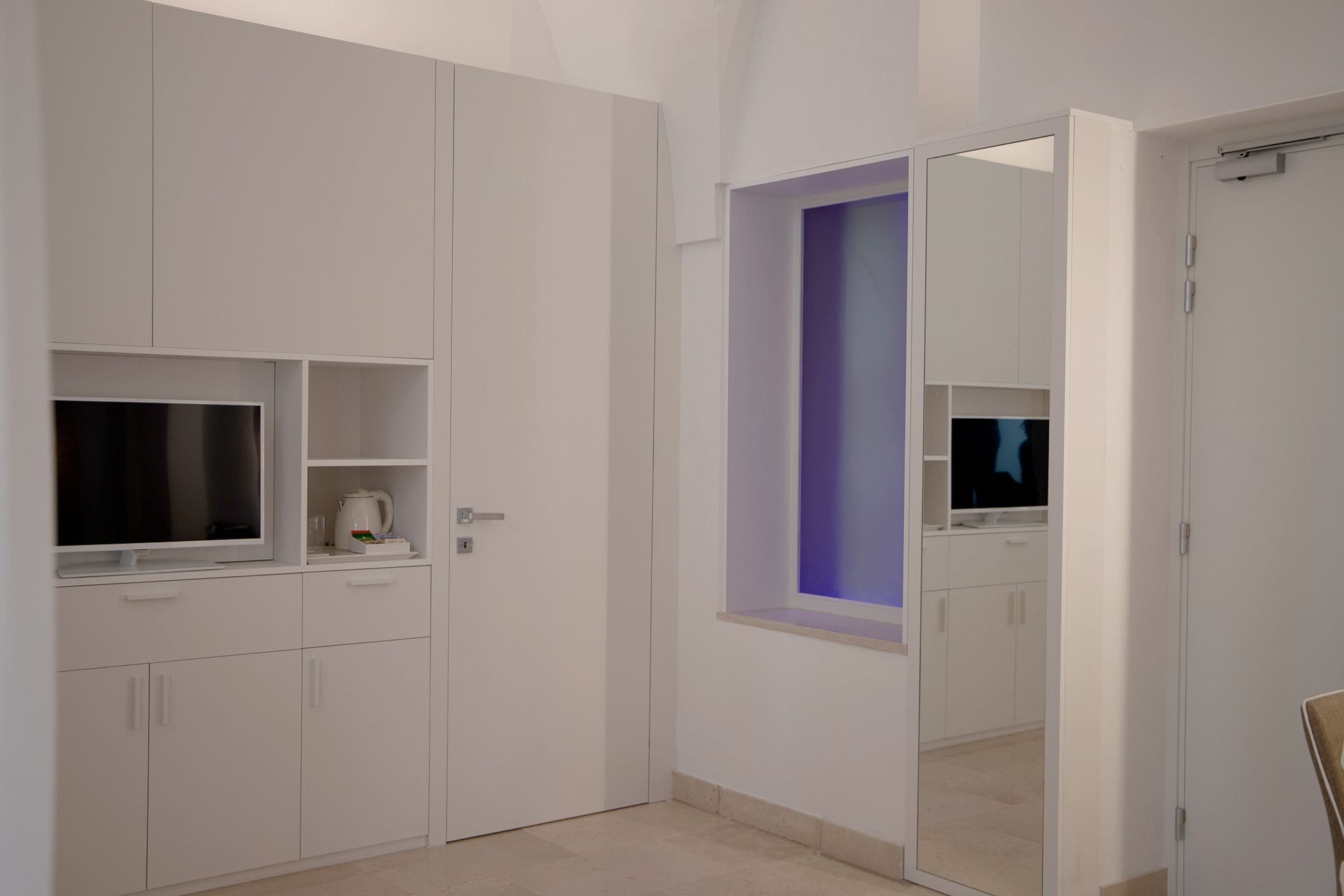Een moderne, minimalistisch ingerichte kamer met witte kasten, een flatscreen televisie en een spiegel.