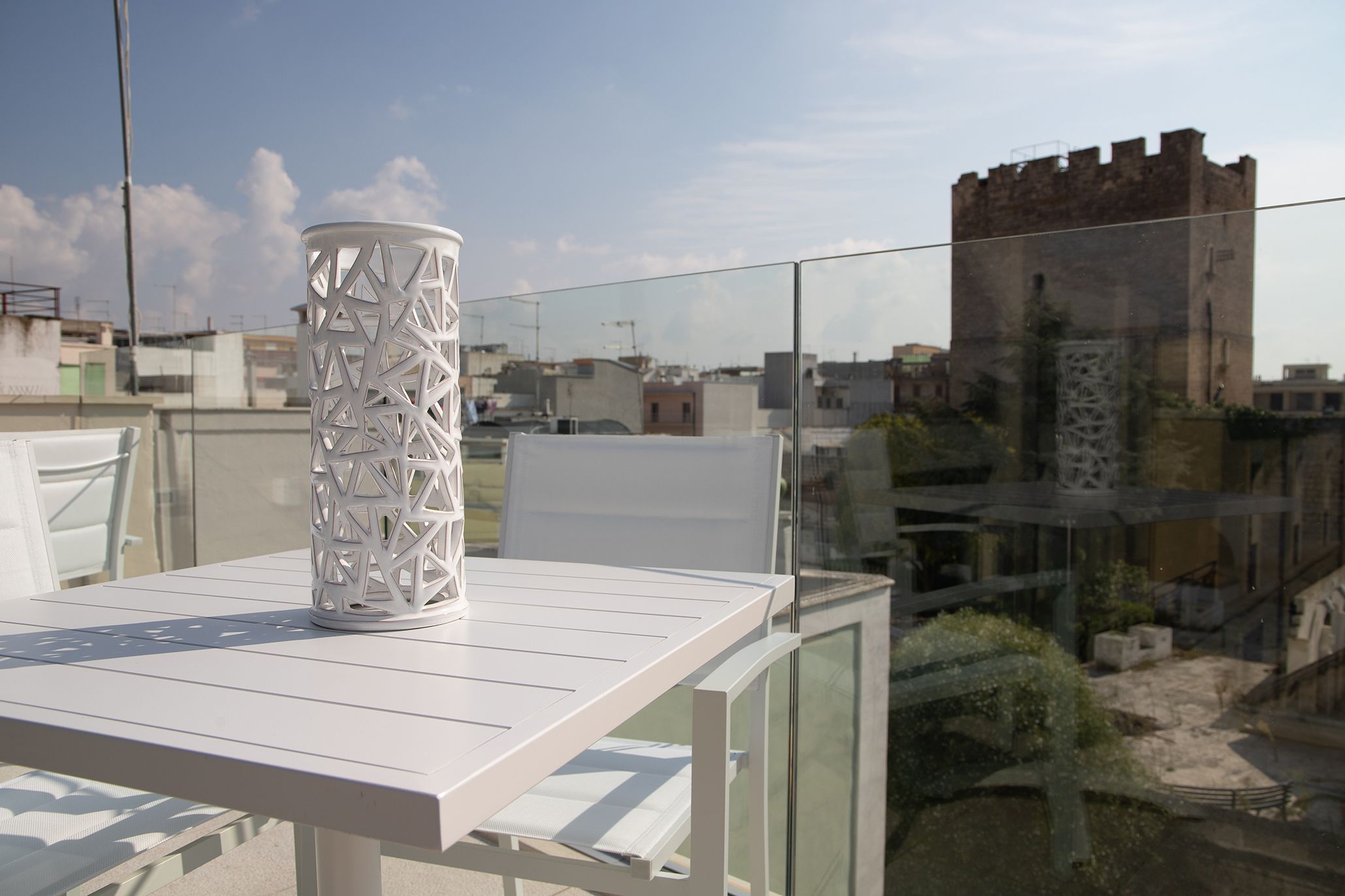 A white table with a decorative white vase on it, overlooking a cityscape with a castle-like structure in the background.
