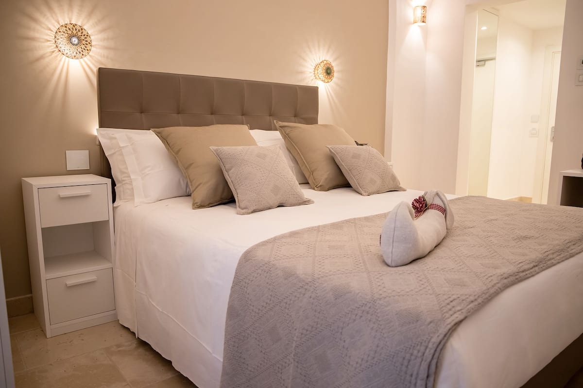 A neatly made bed with a headboard, two bedside tables, and wall-mounted lights.