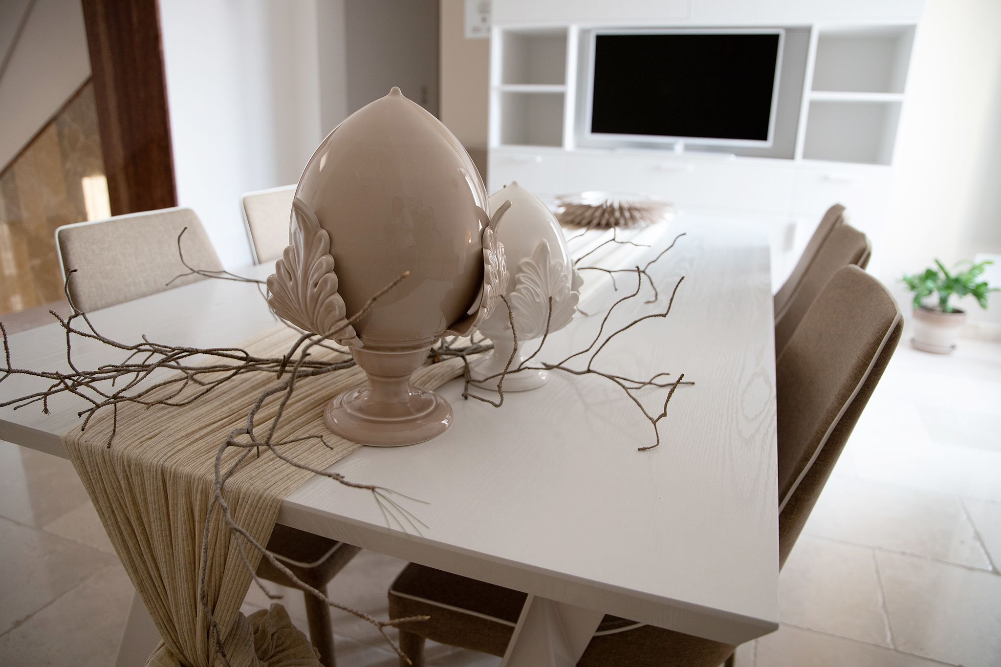 A dining table with chairs, a vase, and decorative branches.