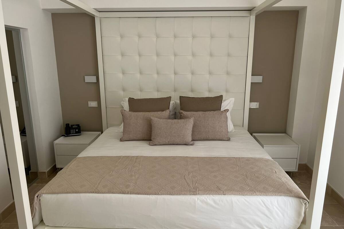 A neatly arranged bedroom with a large bed, two bedside tables, and a padded headboard.
